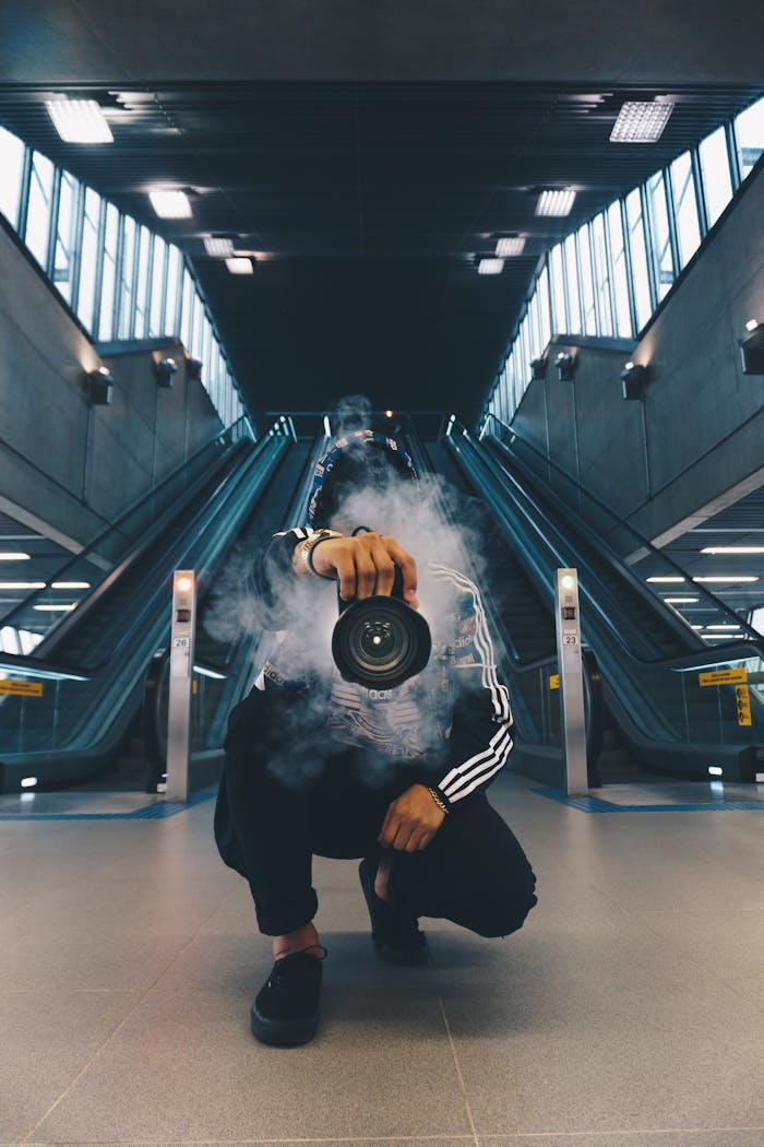 Person holding a camera in a smoke-filled urban setting with escalators.